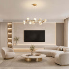 A lit Clérachic ceramic petal chandelier above a living room with a curved sofa, a swivel chair and a wall-mounted TV.