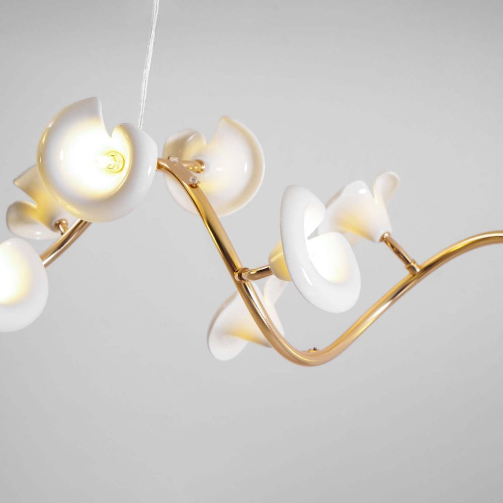 Close view of curled white ceramic petals, each with a bulb inside, on the twisting gold arm of this Clérachic chandelier.