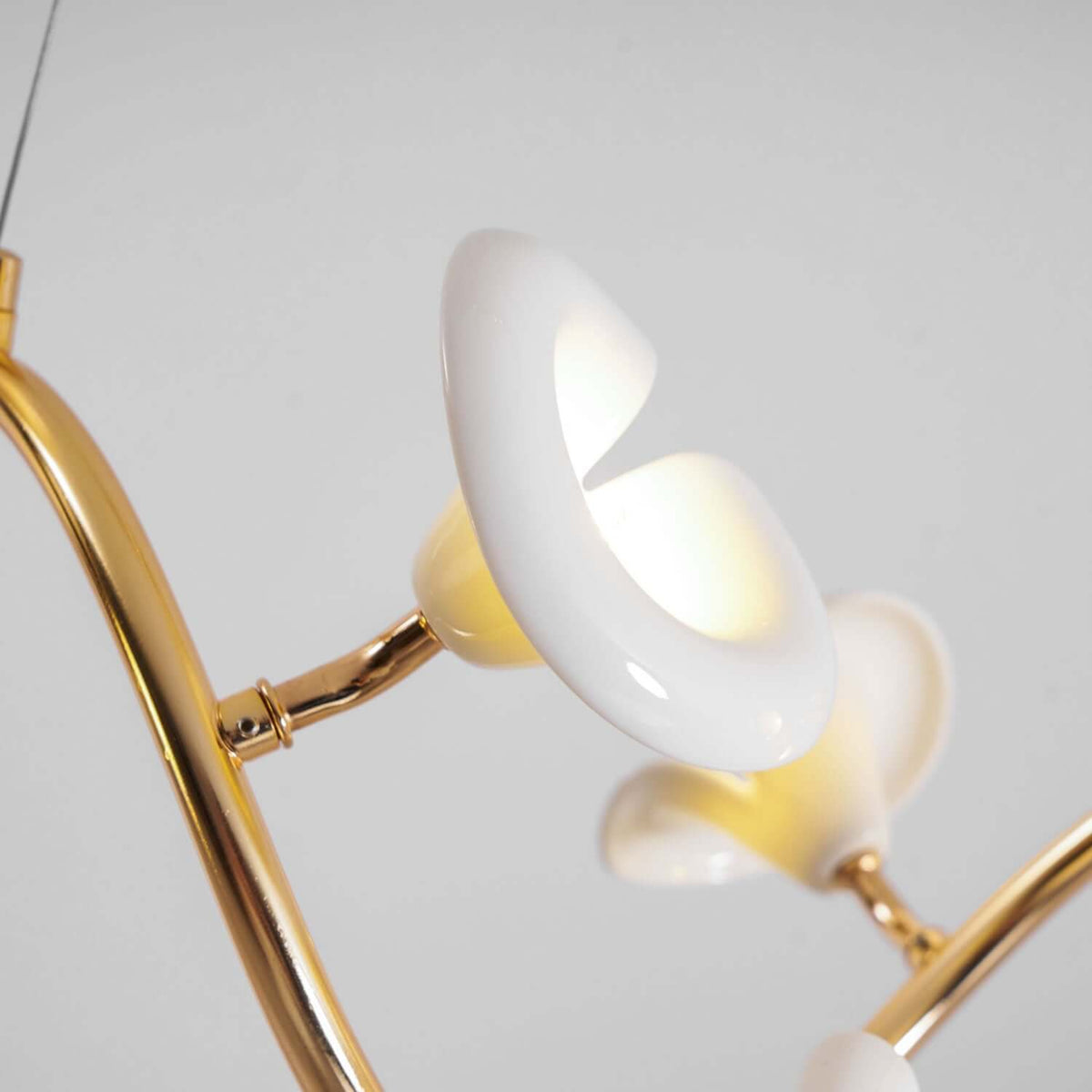 Close view of a glossy ceramic petal and the gold stem it sits on, from this Clérachic chandelier, against a plain grey backdrop.
