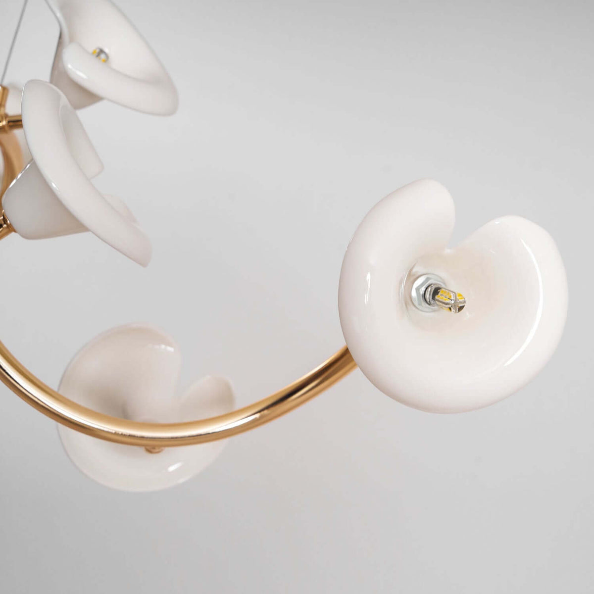Close view of a glazed ceramic petal with its small LED bulb, and the curving gold arm of this Clérachic chandelier.