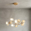 The round Clérachic chandelier hanging below a gold ceiling plate on thin wires, its ceramic petals lit against a grey limewash wall.
