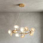 The round Clérachic chandelier hanging below a gold ceiling plate on thin wires, its ceramic petals lit against a grey limewash wall.