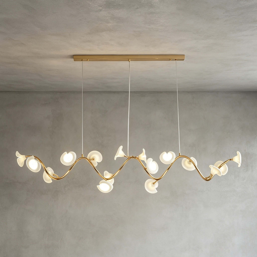 A Clérachic linear chandelier in its longer form, with petals along a wavy gold arm below a slim gold ceiling bar on grey limewash.