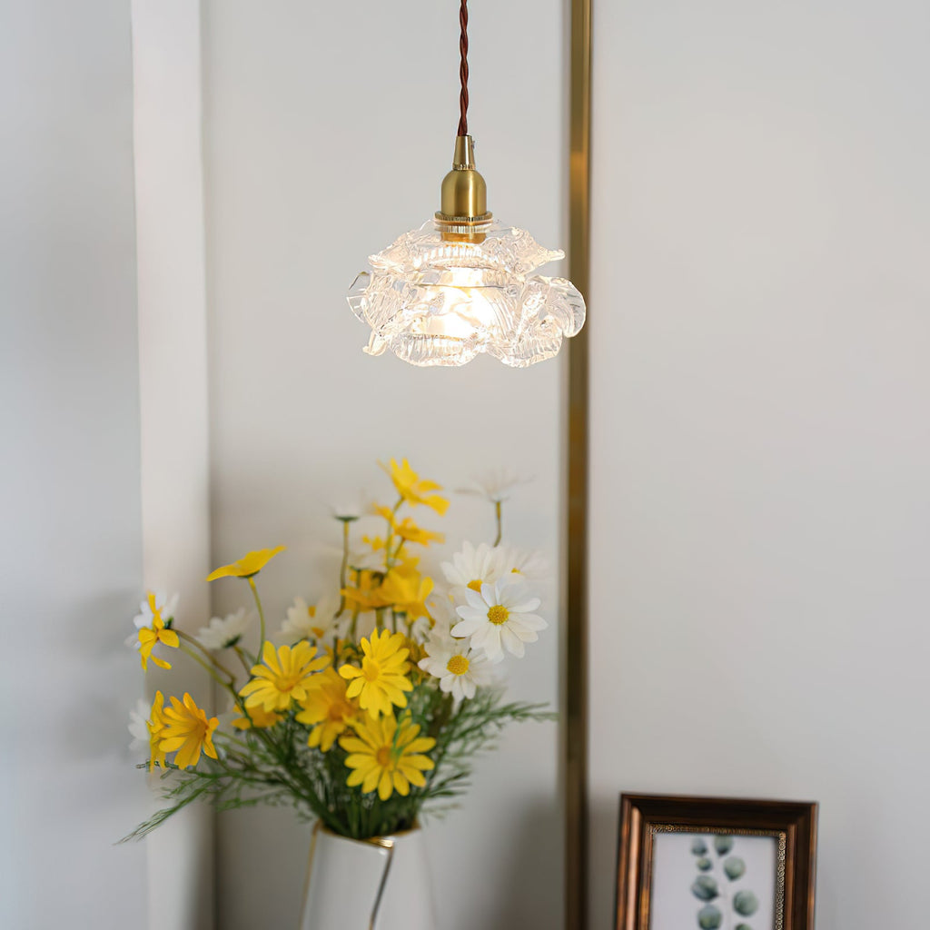 A rose-shaped glass shade from Clérachic hangs on a twisted cord beside a vase of yellow daisies and a small framed print.