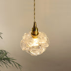 Close view of the frilled glass petals around the bulb of this Clérachic wall light, with its brass cap and twisted cord above.