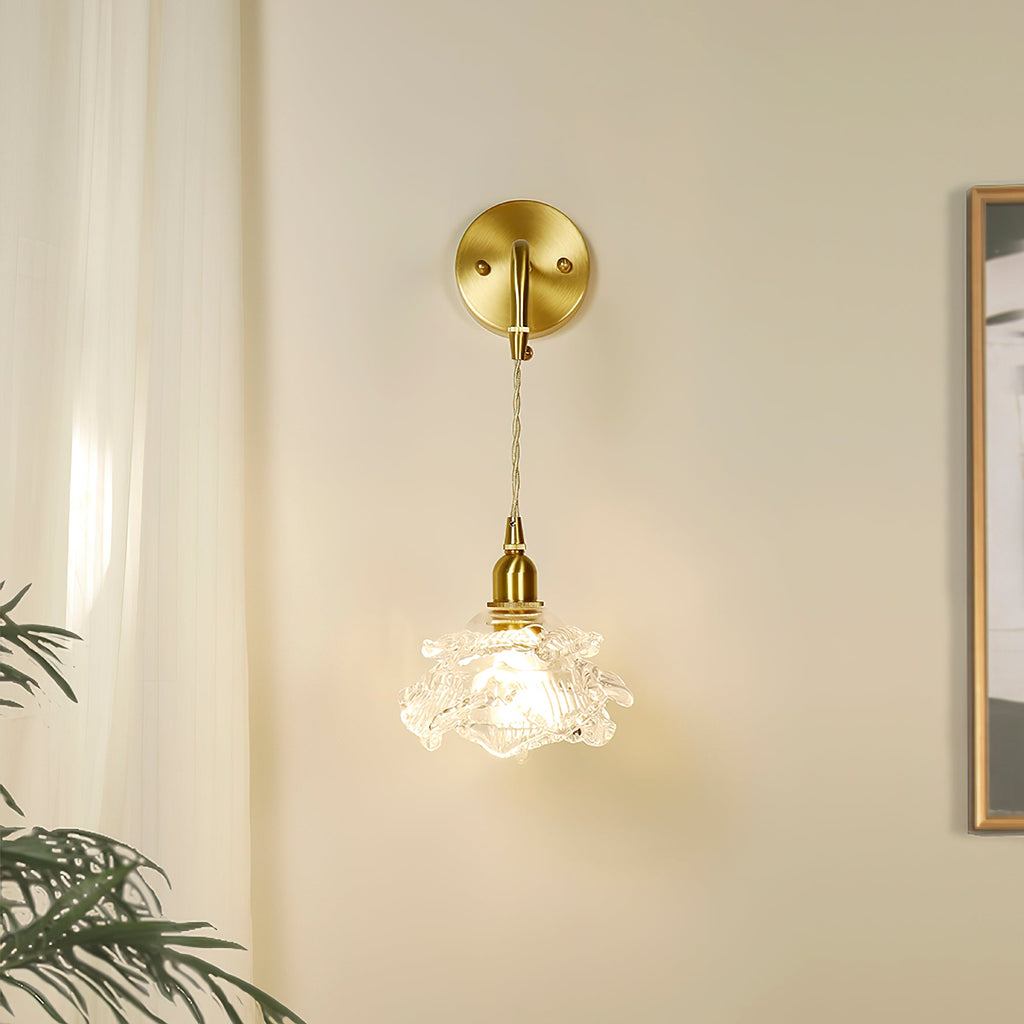 By a cream curtain and a framed picture, this Clérachic wall light hangs its small glass rose shade from a round brass plate.