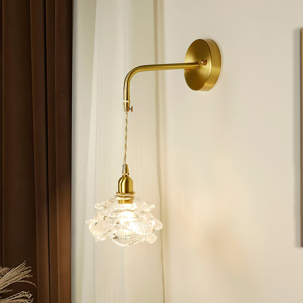 Rose-shaped glass shade on a twisted cord below a bent brass arm, on this Clérachic wall light against a white curtain.
