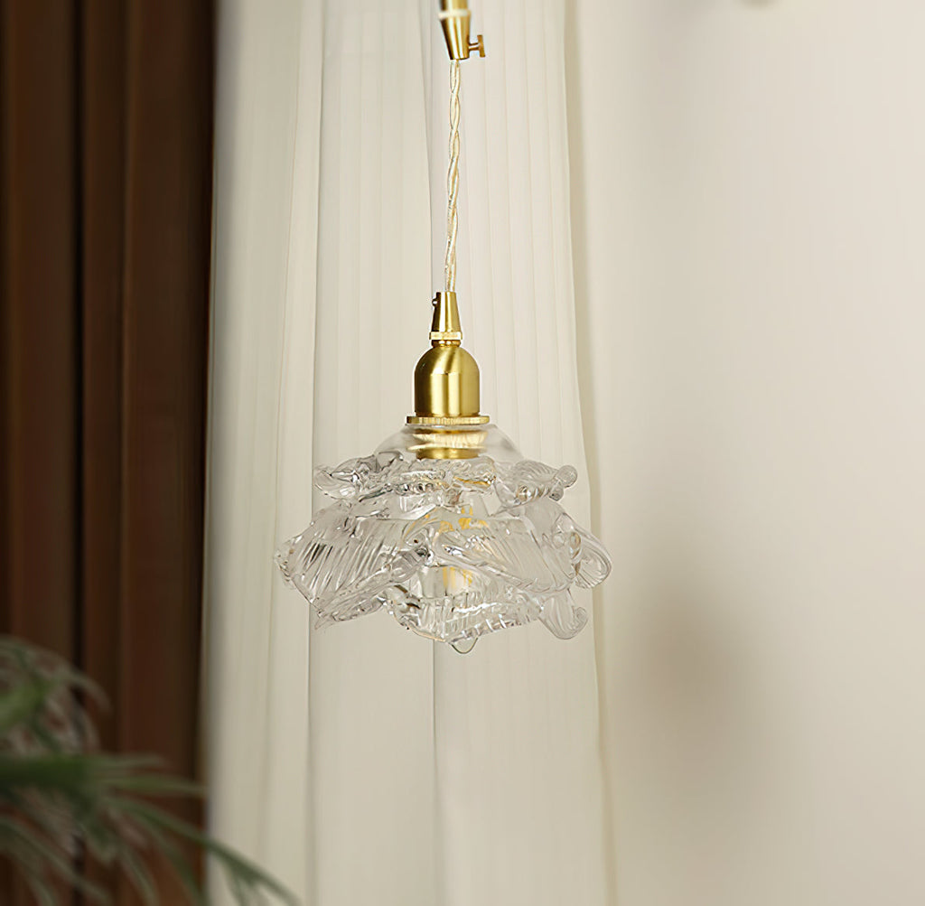 Unlit and clear, the ruffled glass shade of this Clérachic wall light hangs below its brass holder against a white curtain.