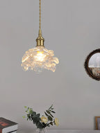 Lit glass rose shade on a brass holder, from this Clérachic wall light, against a grey wall with a small round mirror.