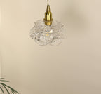 Pale, unlit rose-shaped glass shade on a brass cap and twisted cord, on this Clérachic wall light, against a cream wall.