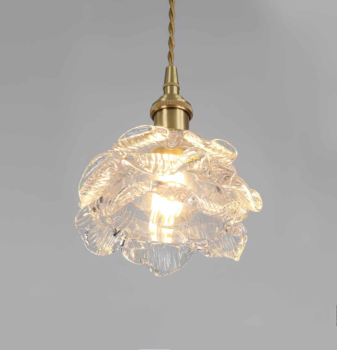 Lit from within, the layered glass petals of this Clérachic wall light shade glow beneath a brass holder on a grey backdrop.