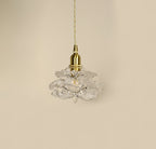 Unlit, the layered clear glass petals and brass cap of this Clérachic wall light hang against a beige wall.