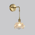 Round brass backplate, curved arm, braided cord and rose glass shade on this Clérachic wall light, on a plain grey backdrop.