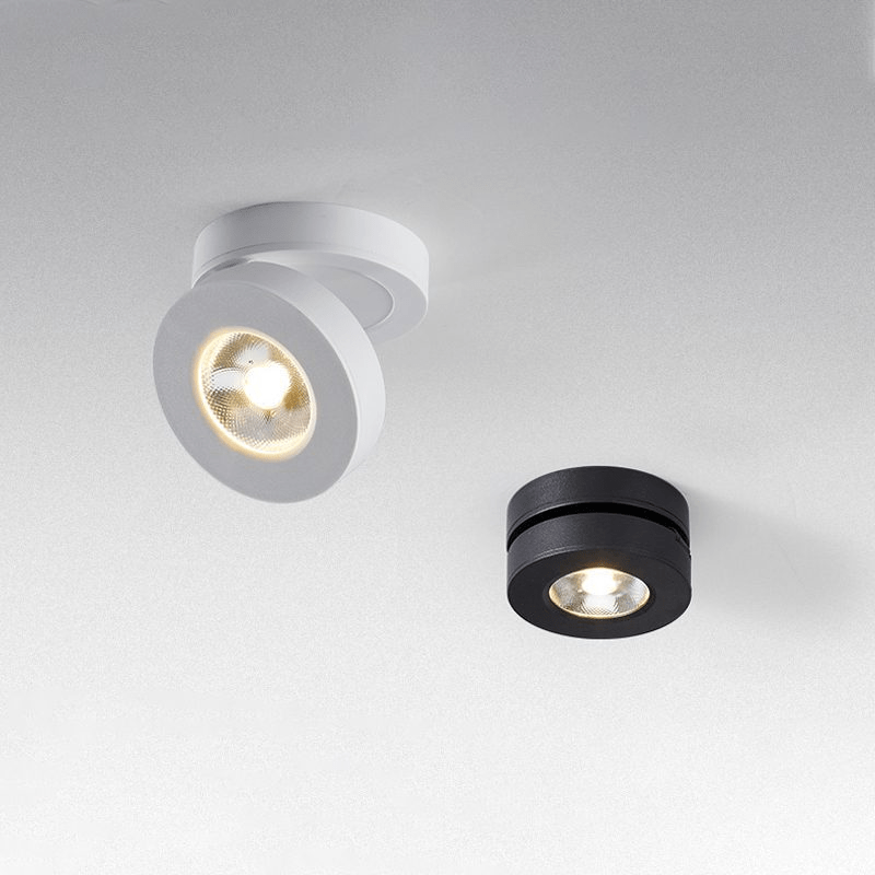A white and a black Clérachic ceiling spotlight side by side on a pale ceiling, the white one tilted, the black one sitting flat.