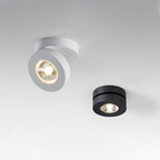 A white and a black Clérachic ceiling spotlight side by side on a pale ceiling, the white one tilted, the black one sitting flat.