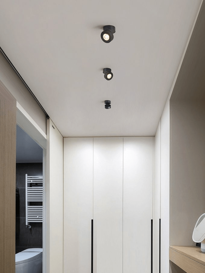 Three small black Clérachic spotlights in a row down a hallway ceiling, beside tall white wardrobe doors with slim black handles.