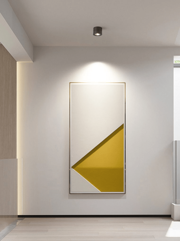 A single dark Clérachic spotlight on a hallway ceiling, washing a large framed abstract print with a pool of warm light.