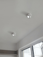 Two white Clérachic spotlights on a sloped white ceiling beside a window, each with its head angled to one side.