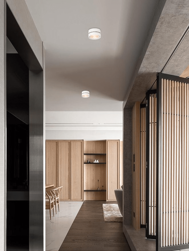 White Clérachic spotlights in a line on the ceiling of a long corridor, with a wood-panelled room and slatted screen at the far end.