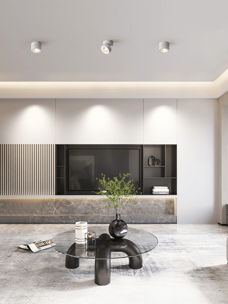 Three small white Clérachic spotlights on the ceiling of a living room, lighting a wall behind a glass coffee table and a slatted panel.