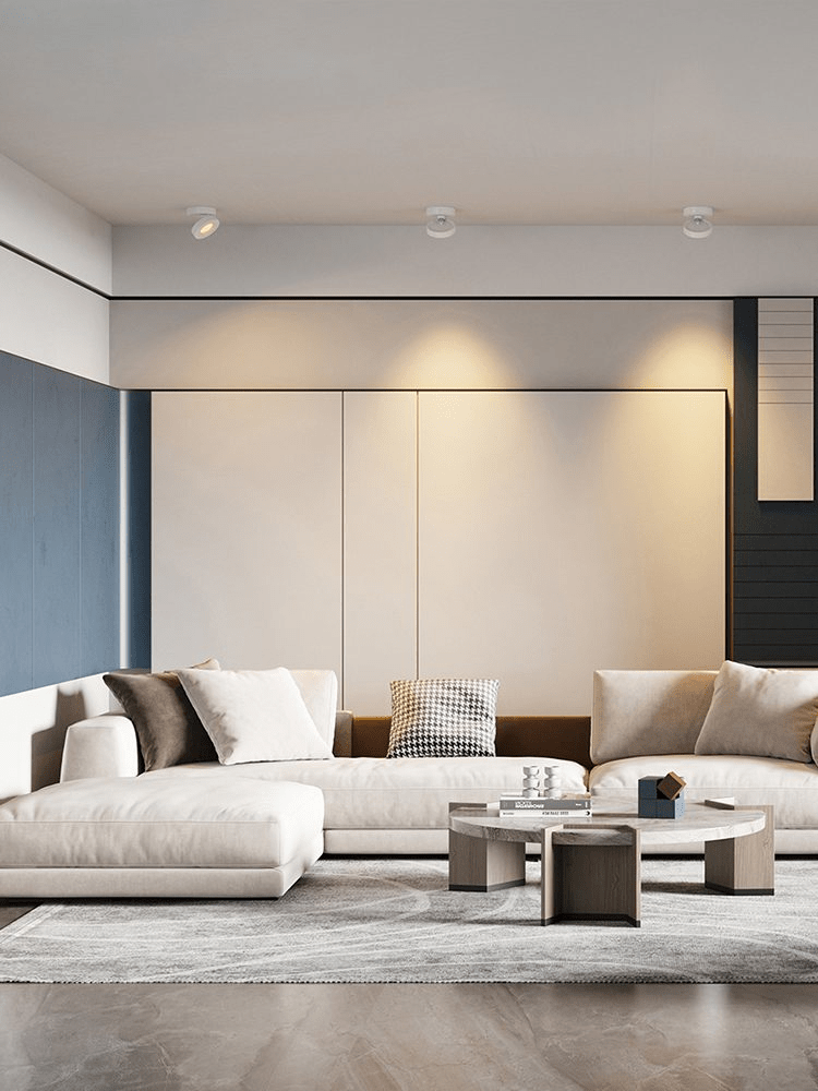Three small Clérachic spotlights along a living room ceiling, each lighting the cream wall above a white sectional sofa.