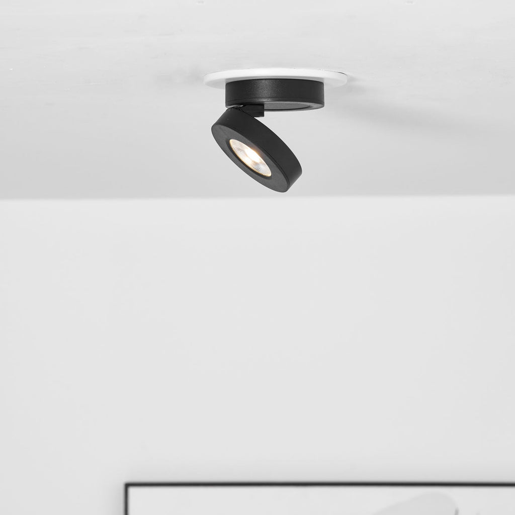 Clérachic black spotlight with its head tipped to one side inside a white ring, above the edge of a framed picture.