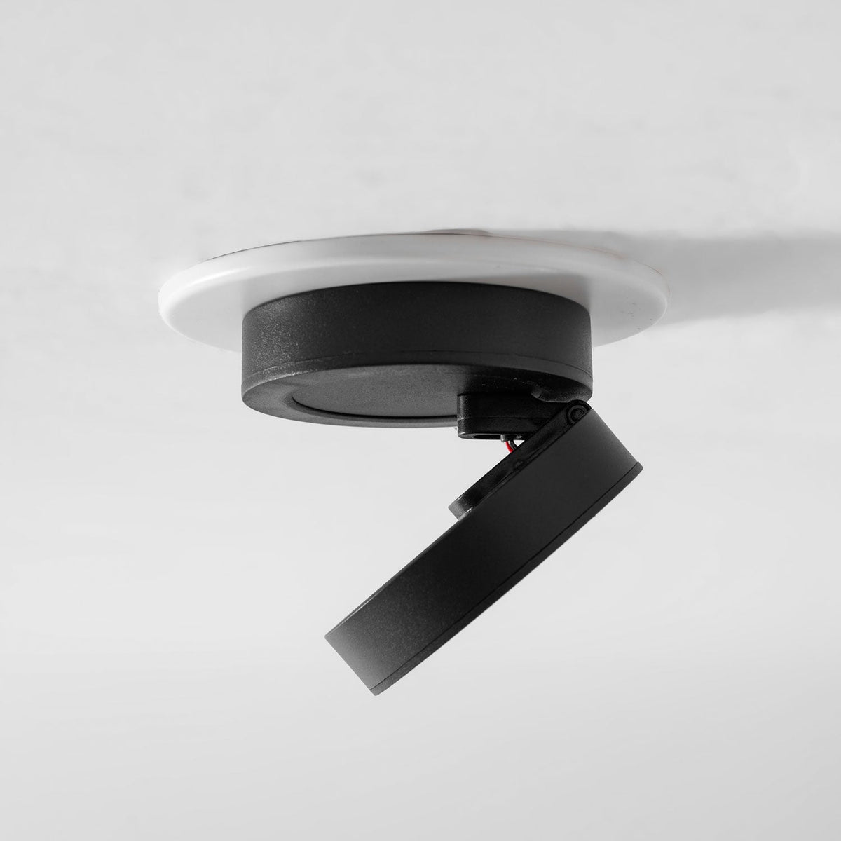 Side view of a black Clérachic spotlight in a white ring, with its disc head swung out below the cylindrical base.