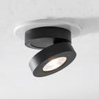 Black Clérachic spotlight with its head tilted well out from the base and its LED lit warm, set into a white ceiling ring.