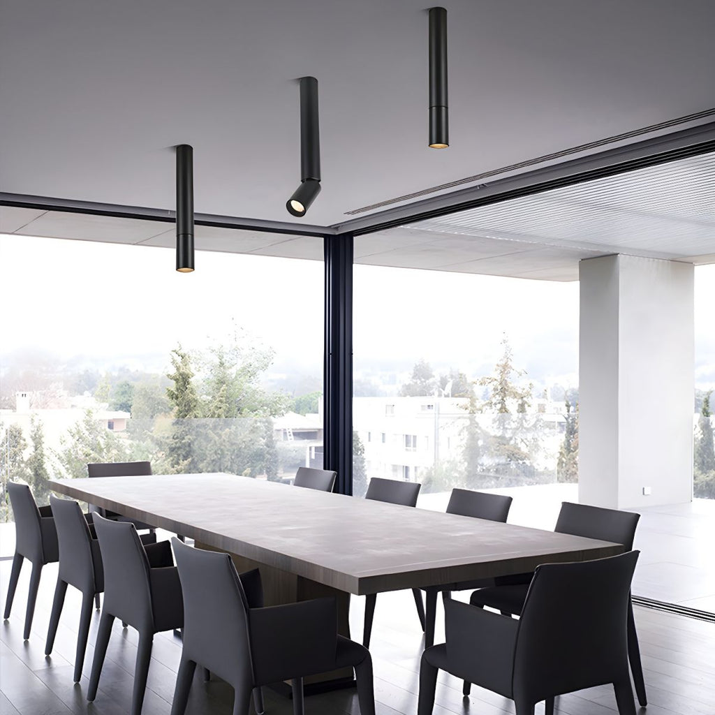 Three black Clérachic spotlights hang at different lengths over a long dining table, in front of floor-to-ceiling glass.