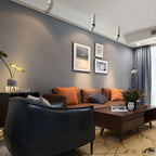 White Clérachic ceiling spotlights of different lengths line a grey-blue wall above a sofa with orange cushions.
