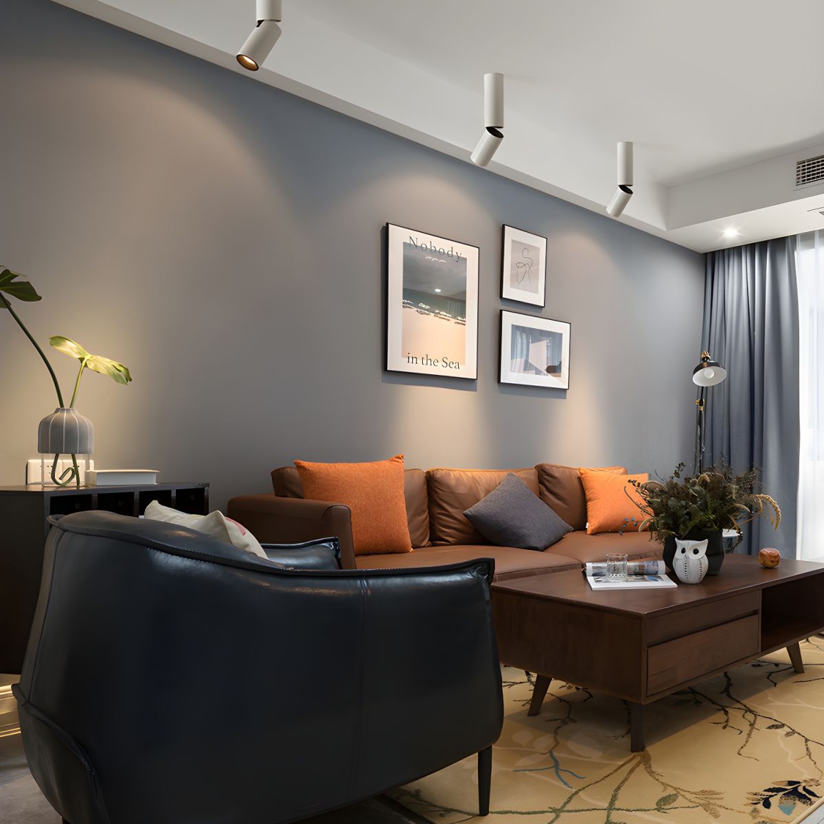 White Clérachic ceiling spotlights of different lengths line a grey-blue wall above a sofa with orange cushions.