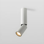 Short white Clérachic ceiling light with its head tilted and a warm glow in the lens, on a light grey background.