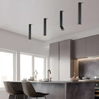 Four black Clérachic spotlights in different lengths hang above a kitchen island with grey stools, one with its head angled.