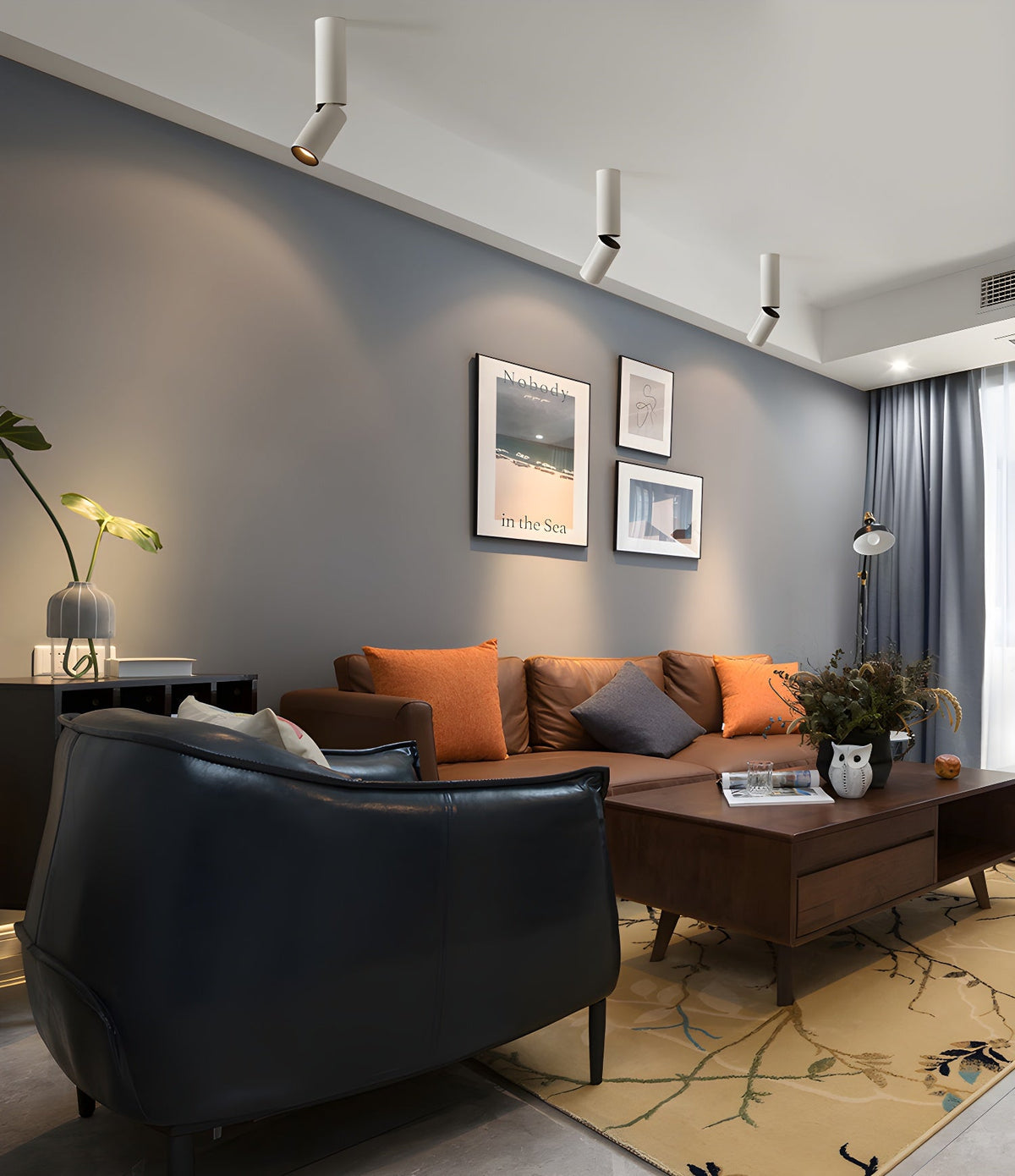 A row of white Clérachic spotlights runs across the ceiling over a leather armchair and a sofa with orange cushions.