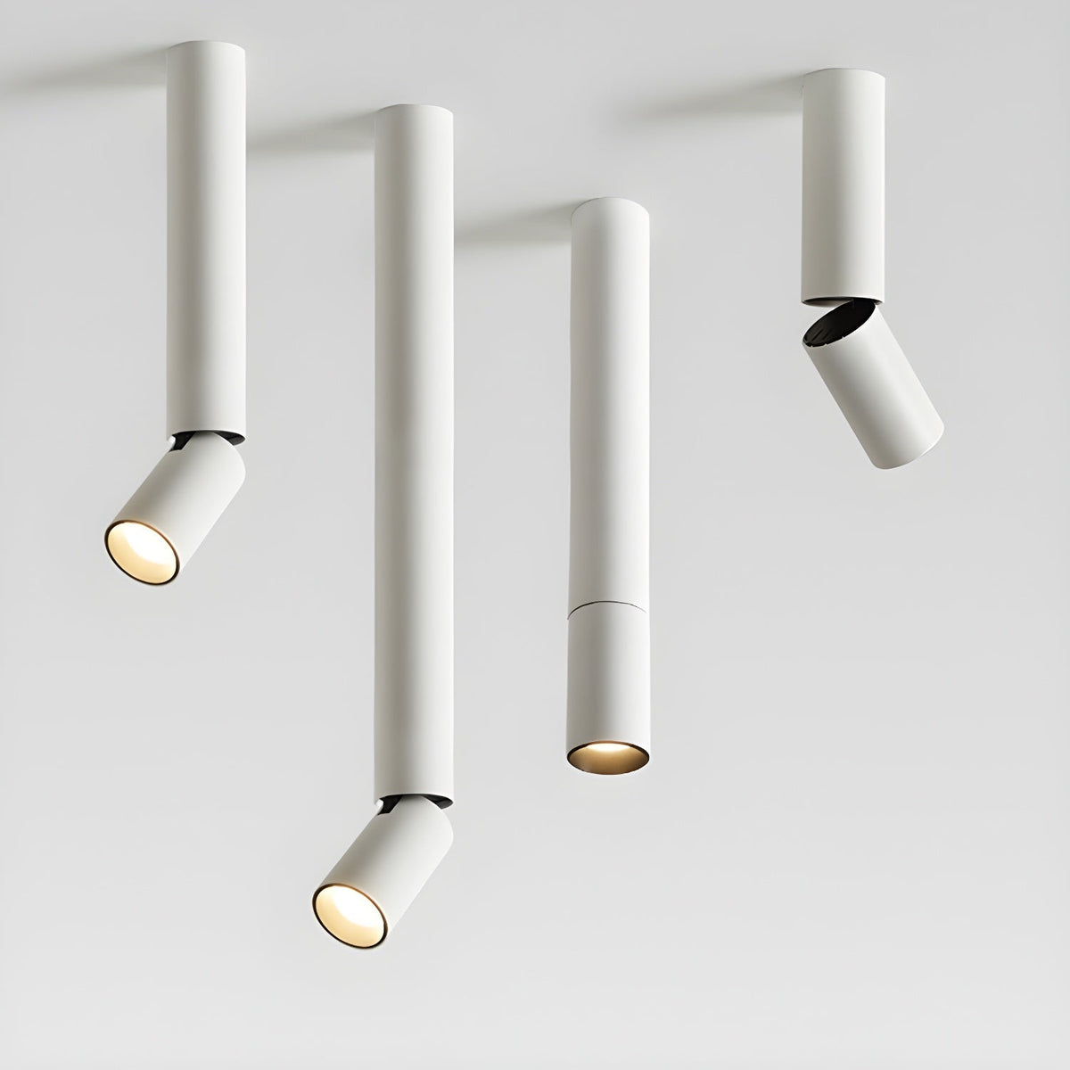 Four white Clérachic spotlights in different pole lengths on a pale backdrop, three with angled heads and one with a straight head.