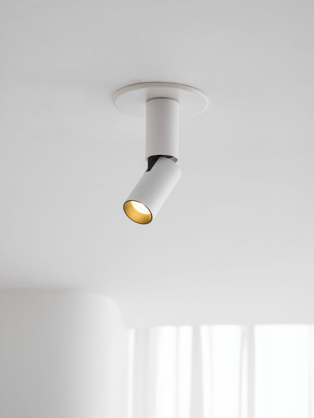 This white Clérachic spotlight sits in a flat round ceiling plate, its angled head showing a gold-toned inner ring.