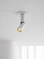 This white Clérachic spotlight sits in a flat round ceiling plate, its angled head showing a gold-toned inner ring.