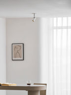 Tiny from a distance, this white Clérachic spotlight sits on a ceiling above a framed print and a table with a book and glass.