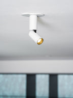A white Clérachic spotlight in a round ceiling plate, its head turned aside, with a glass-fronted shelf blurred behind.