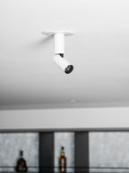 A smaller view of this white Clérachic spotlight, its black lens ring and joint visible, beside blurred shelves of bottles.