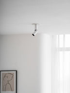 A white Clérachic spotlight on the ceiling, its head pointing down towards the left, above a framed line drawing.