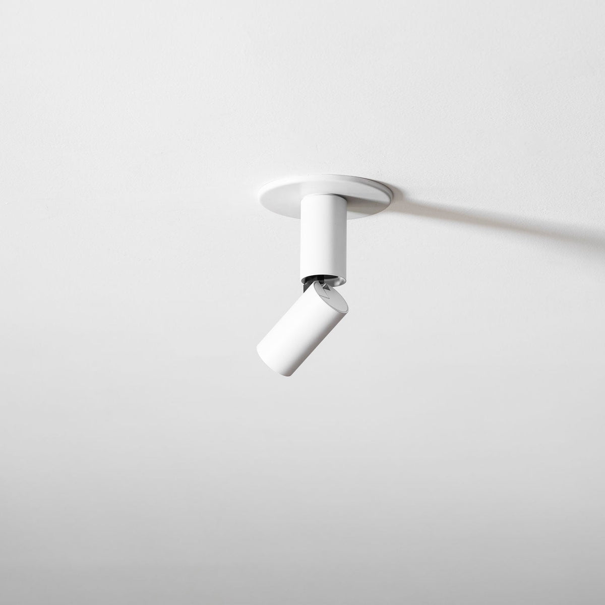 White Clérachic spotlight on a white ceiling, its slim head swung away at an angle, casting a soft shadow.