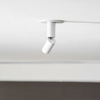A white Clérachic spotlight with its head swung out at an angle, set against a white ceiling and a dark wall below.