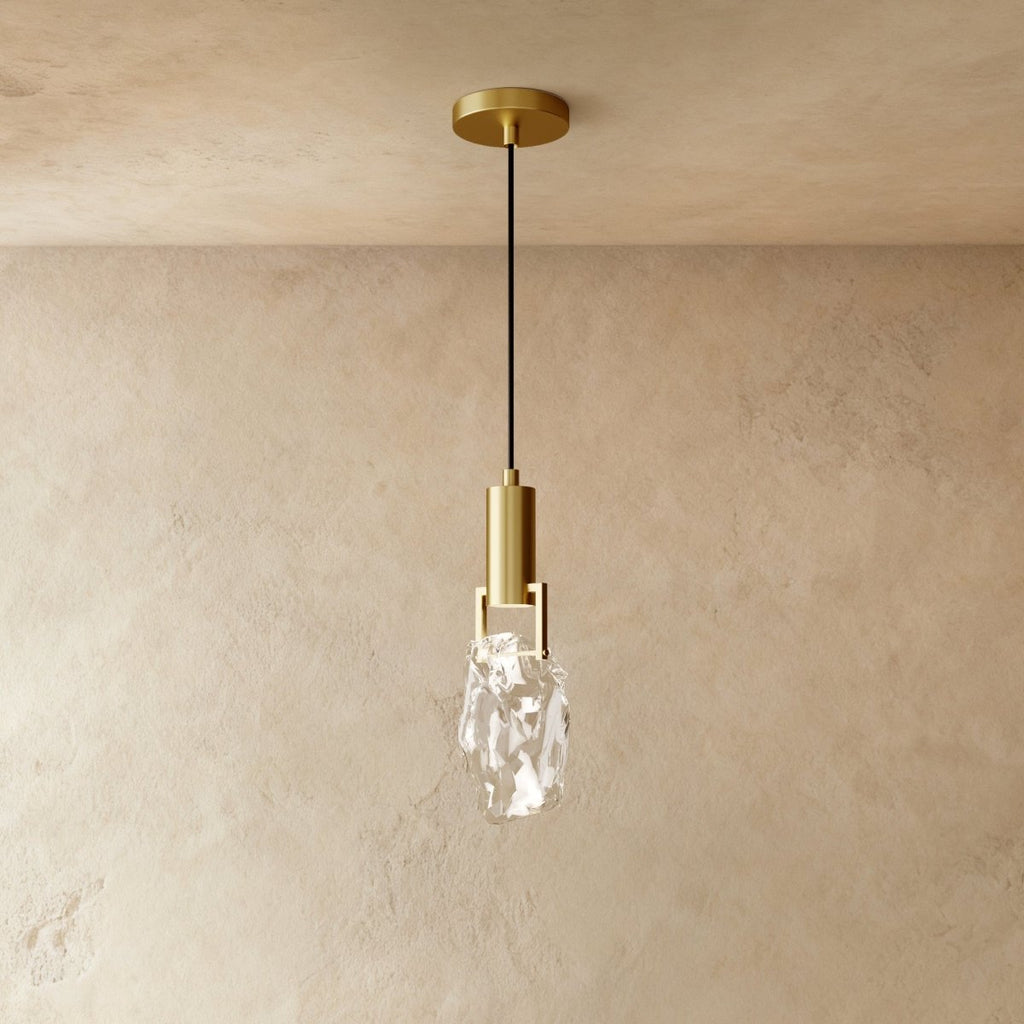 A Clérachic brass pendant holds a rough-cut clear crystal glass shade in a brass bracket against plastered walls.
