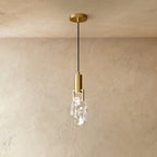 A Clérachic brass pendant holds a rough-cut clear crystal glass shade in a brass bracket against plastered walls.