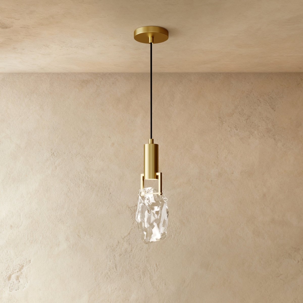 A Clérachic brass pendant holds a rough-cut clear crystal glass shade in a brass bracket against plastered walls.