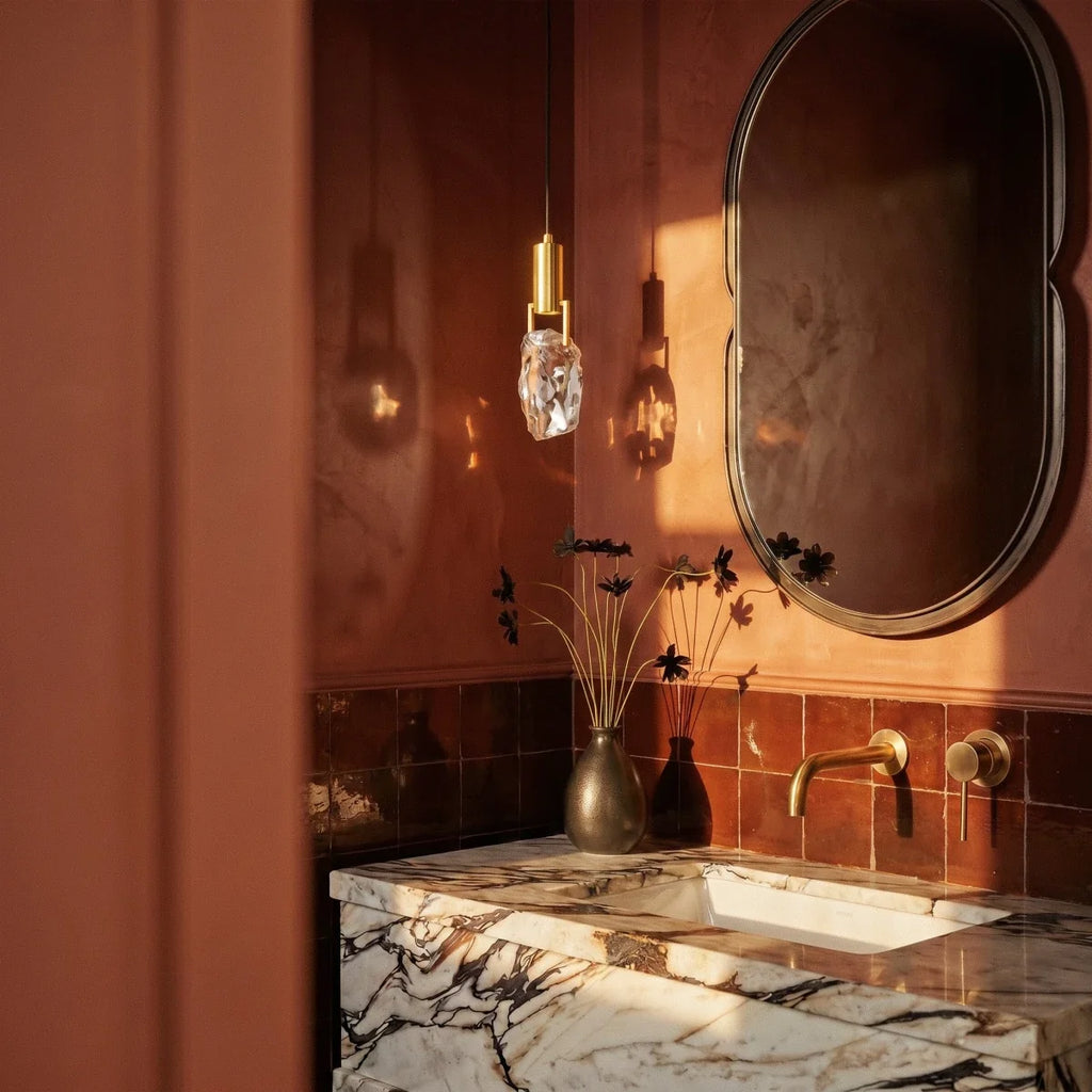 This Clérachic crystal pendant lights a terracotta powder room beside a scalloped mirror and veined marble sink.