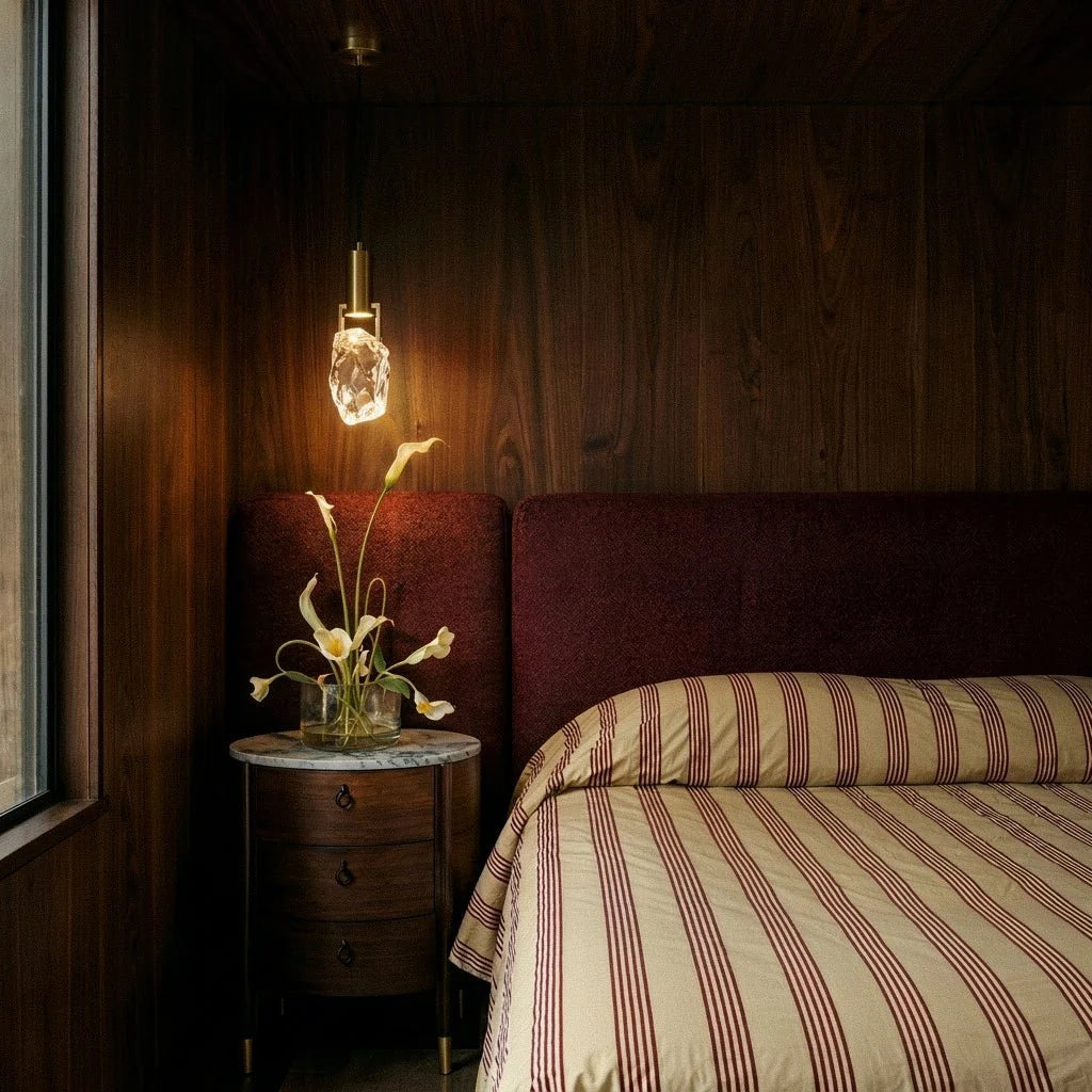 A Clérachic crystal pendant lights a walnut-paneled bedside nook above a striped bed and round nightstand.