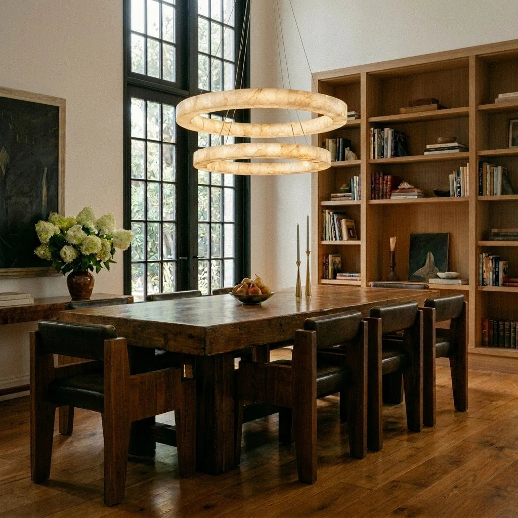 Clérachic two-tier alabaster chandelier glowing above a rustic dining table beside a built-in bookshelf.