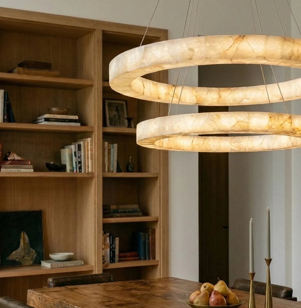 Clérachic alabaster chandelier detail, its two stacked rings glowing warm near a wooden bookshelf backdrop.